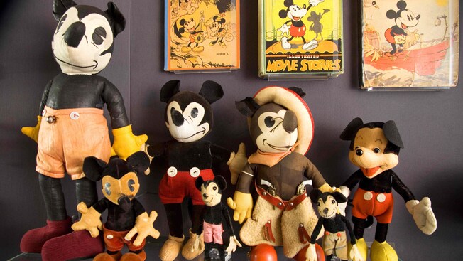 A collection of 7 Mickey Mouse plush toys from different eras under mounted, vintage Mickey publications