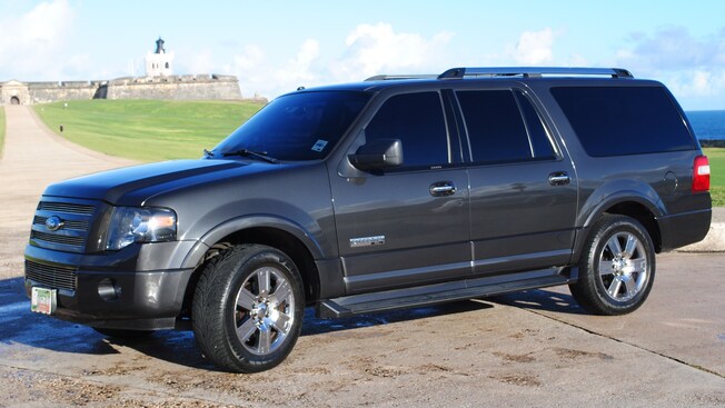A large SUV with tinted windows sits on a path leading to a stone fort