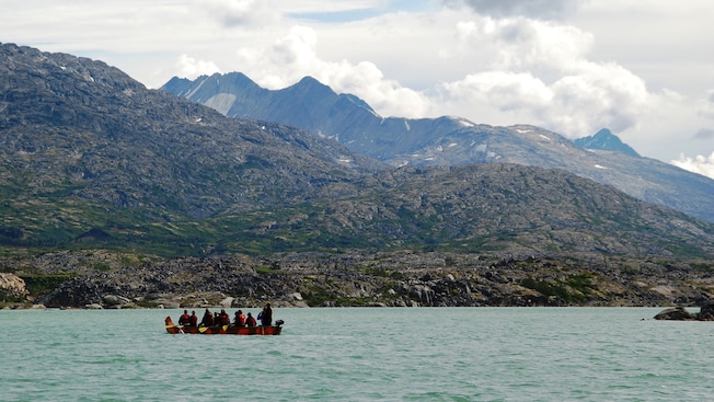 Guests in a motorized canoe stop to look out to the mountainous landscape