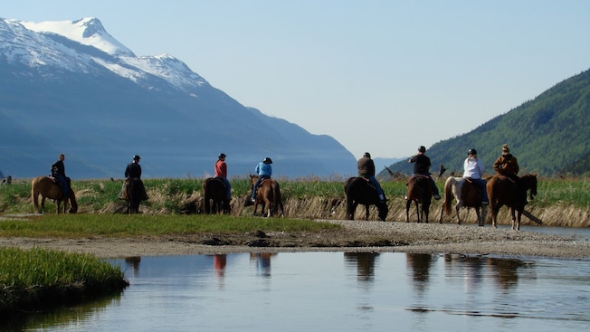 Un pequeño grupo de jinetes se detiene en un arroyo de poca profundidad en el fondo del valle Un pequeño grupo de jinetes se detiene en un arroyo de poca profundidad en el fondo del valle