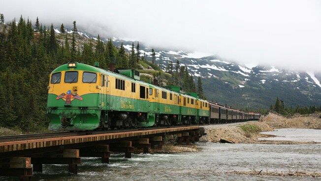 A vintage train rolls along the tracks over a shallow lake in the mountains