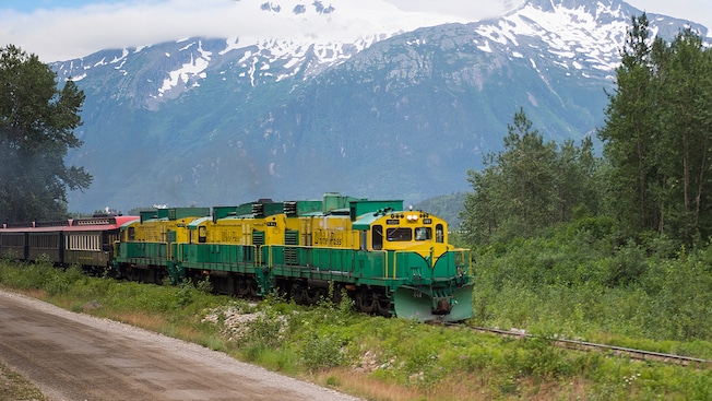 A train travels through a forest against the backdrop of a snowy mountain A train travels through a forest against the backdrop of a snowy mountain