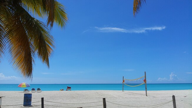 Three beach chairs sit next to a volleyball net on an empty beach