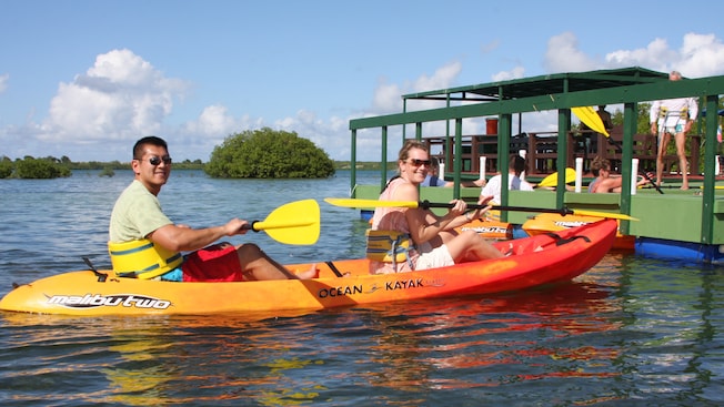 Two people sitting on a kayak at a wooden dock smile at the camera with paddles in their hands Two people sitting on a kayak at a wooden dock smile at the camera with paddles in their hands
