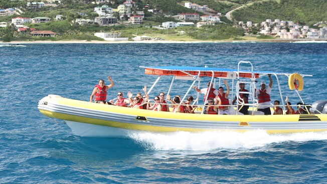 Passengers wave from a rigid hull inflatable boat as they cruise along the shoreline
