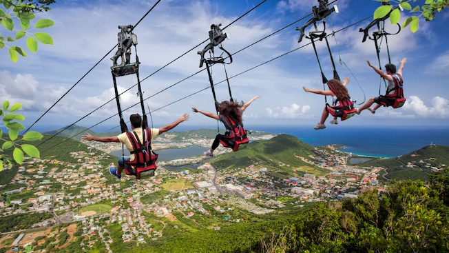 4 people strapped into harnesses on zip lines above a forested island 4 people strapped into harnesses on zip lines above a forested island