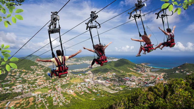 4 people strapped into harnesses on zip lines above a forested island 4 people strapped into harnesses on zip lines above a forested island