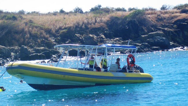 Passengers preparing to go snorkeling from a rigid inflatable powerboat moored near a rocky coastline
