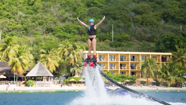 Una mujer en una tabla aerodeslizadora extiende las manos mientras es impulsada en el aire por una manguera larga conectada a un jet ski
