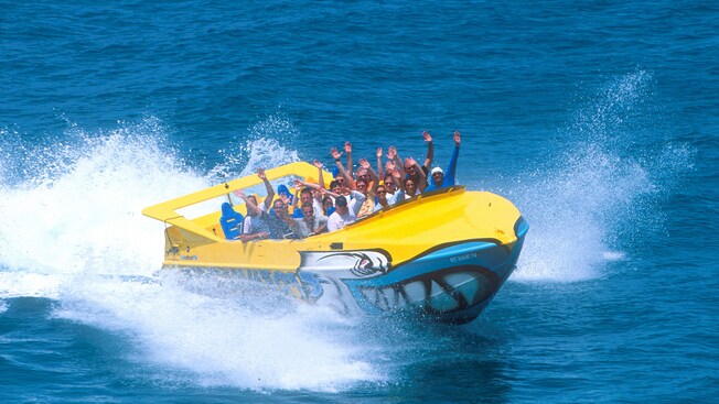 A speedboat filled with passengers has a shark design on its bow