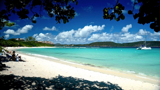 A white sand beach with Guests relaxing and a catamaran close to the shore A white sand beach with Guests relaxing and a catamaran close to the shore