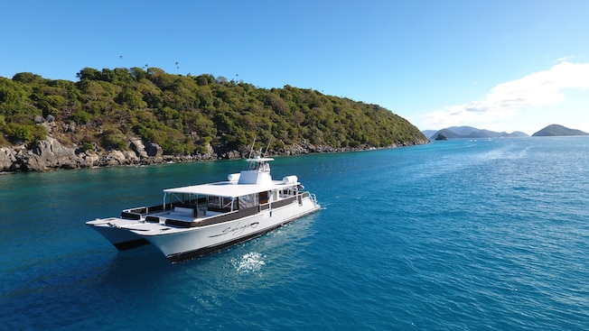 A catamaran floats near a forested shore near a chain of islands A catamaran floats near a forested shore near a chain of islands