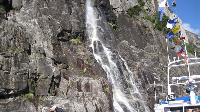 A catamaran cruising close to a steep mountainside with a cascading waterfall A catamaran cruising close to a steep mountainside with a cascading waterfall