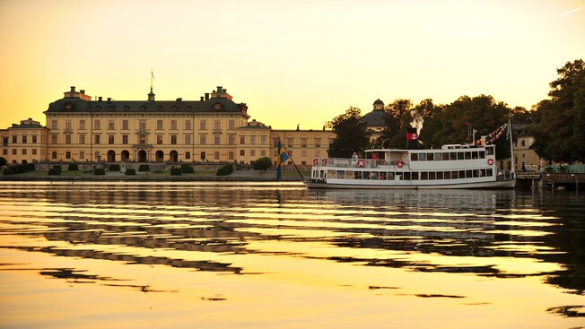 A boat floating on a body of water near a building and trees