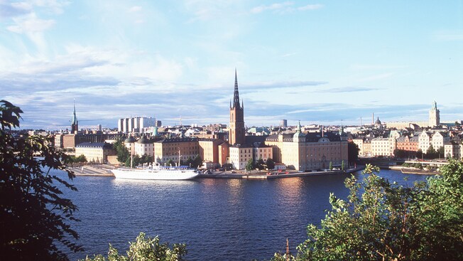 A boat harbor fronts a crowded city with a few church spires protruding above the rest of the buildings