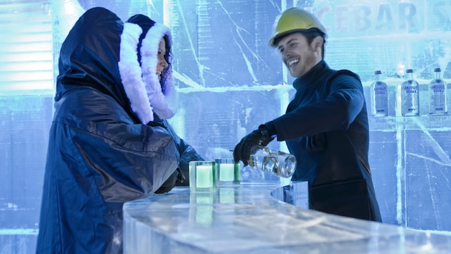 A bartender serving 2 people in a bar made entirely of ice A bartender serving 2 people in a bar made entirely of ice