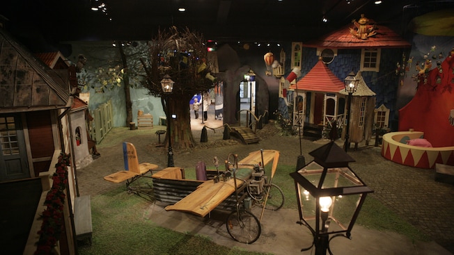 An antique, wooden airplane model is surrounded by models of houses with grass and trees An antique, wooden airplane model is surrounded by models of houses with grass and trees
