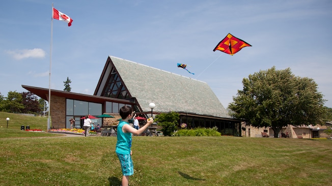 People flying kites on a lawn in front of a building with windows and a vaulted ceiling People flying kites on a lawn in front of a building with windows and a vaulted ceiling