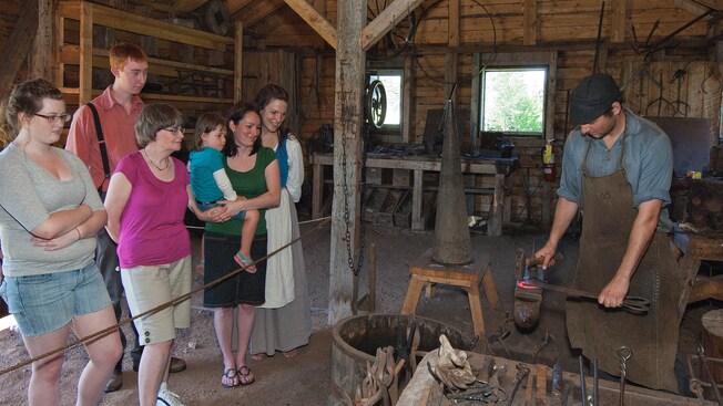 People watch a blacksmith work behind a roped off area