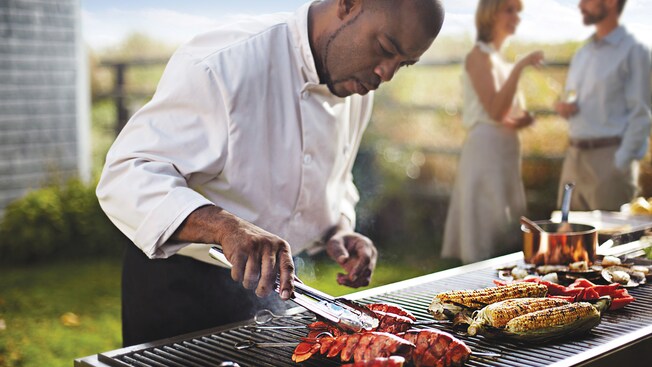 A chef uses tongs to check lobster tails cooking on an outdoor grill