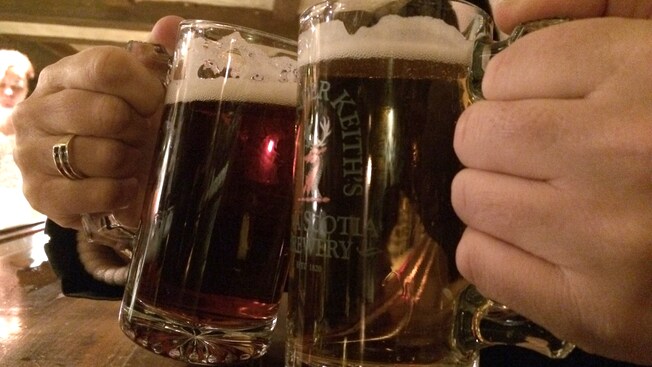 Mugs filled with dark beer are brought together in a toast