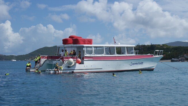 People descend into the water from a snorkel boat, wearing life jackets