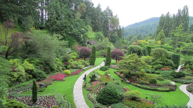 Visitors walking along paths in a sprawling garden while gardeners tend to plants