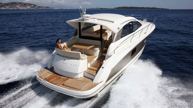 A woman relaxes on a Prestige 42S yacht that floats through the water against the backdrop of a populated peninsula