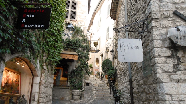 Letreros colgantes de tiendas en un callejón de una ciudad Francesa con edificios antiguos de ladrillo y escaleras que llevan a más tiendas Letreros colgantes de tiendas en un callejón de una ciudad Francesa con edificios antiguos de ladrillo y escaleras que llevan a más tiendas