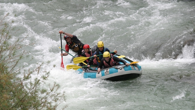 A group of people in an inflatable raft paddle through white water on a river A group of people in an inflatable raft paddle through white water on a river