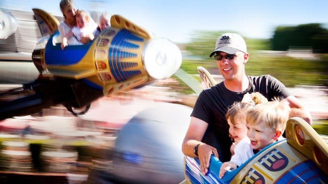 A father and his 2 young kids smile from their spinning Astro Orbitor retro rocket