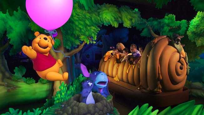 Pooh Bear floats with a balloon above Eeyore and Gopher while Guests travel in a giant honey pot