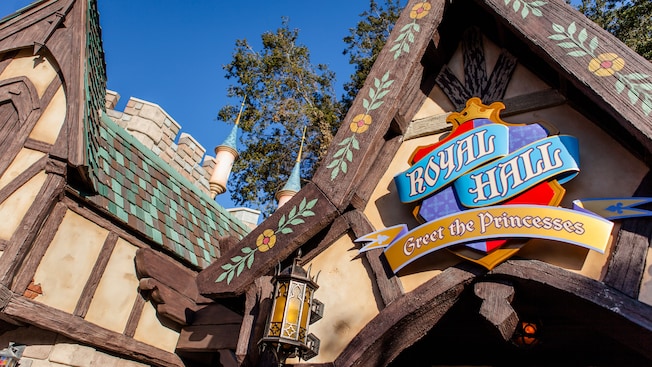 Surrounded by trees, turrets and shingles, a medieval sign reads Royal Hall, Greet the Princesses, on the building’s gable roof