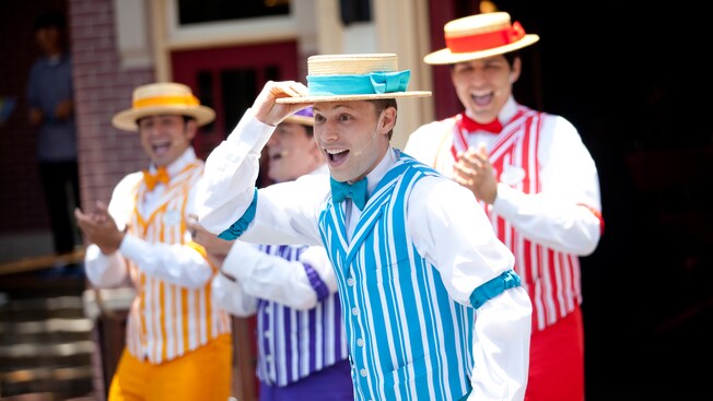 A group of 4 men sing and perform outside wearing boater hats, arm garters and striped vests