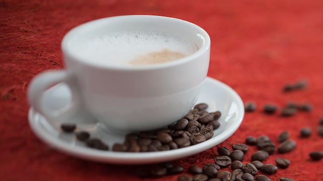 Taza de capuchino con granos de café esparcidos en un platillo y en la mesa