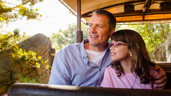 Una hija y su padre sentados en un autobús de safari descubierto miran hacia la jungla 