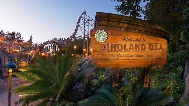 A wooden welcome sign to "DinoLand U.S.A.," with a huge dinosaur skeleton in the background