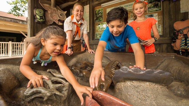 Children touch dinosaur fossils as a smiling Wilderness Explorer Troop Leader watches