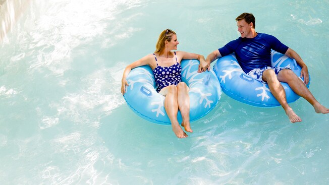 A couple sitting in separate inner tubes holds hands while in Cross Country Creek
