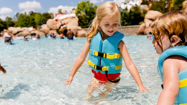 Two young girls wearing lifejackets playing in shallow water at Melt-Away Bay