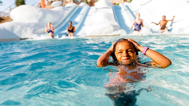 A girl standing in neck-high water of a splashdown pool for 4 waterslides