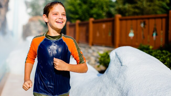 A smiling boy, still wet from his ride down Slush Gusher, jogs at the end of the attraction 