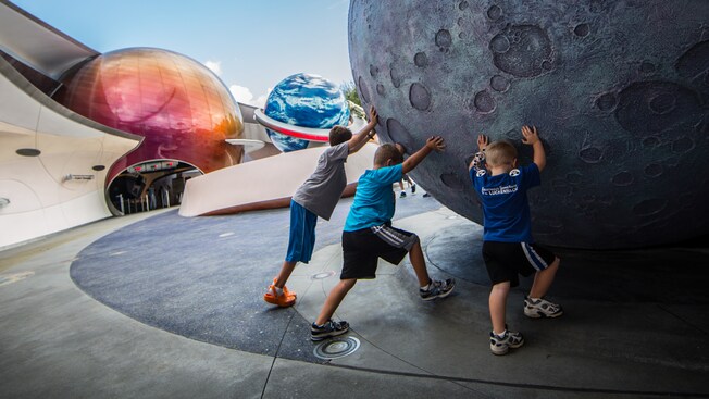Three boys attempt to push a huge sculpture of the moon in Planetary Plaza outside Mission: SPACE