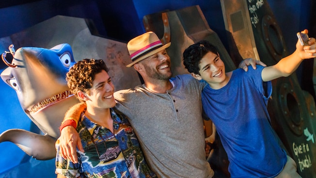 A dad and his 2 teenage sons pose for a photo in front of a shark statue