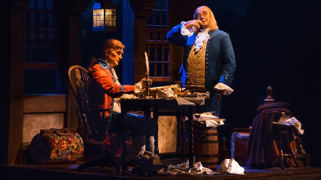 Benjamin Franklin stands across from a seated Thomas Jefferson onstage at The American Adventure