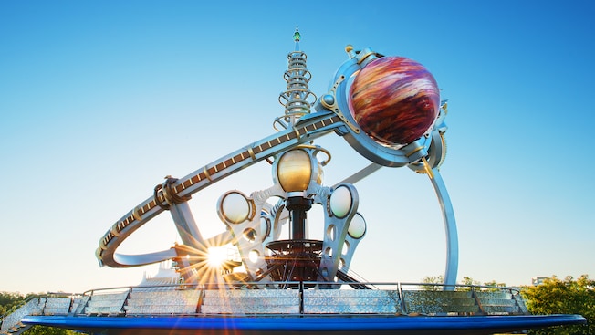 The sun peeks through the metal structure of the Astro Orbiter attraction in Tomorrowland