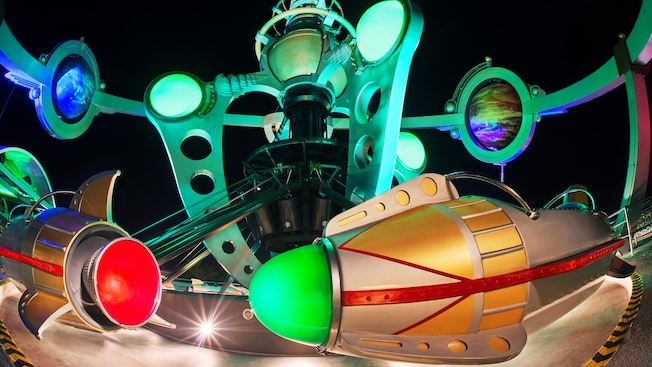 Rocket ships on the Astro Orbiter attraction lit up at night in Magic Kingdom park