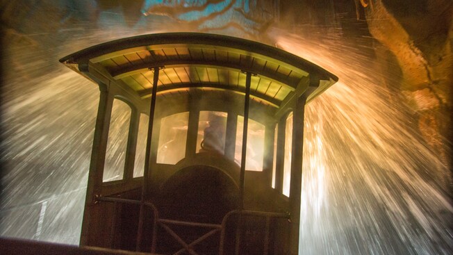 Um trem de mineração passa por um esqueleto de dinossauro exposto na lateral de uma montanha 