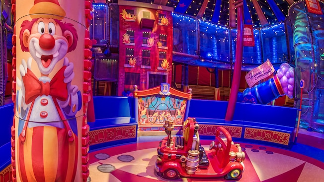 A painting of a clown on a pole and a toy car in the wait area at Dumbo, the Flying Elephant