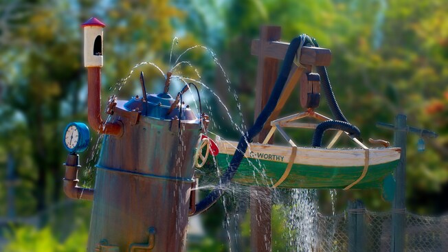A comical pressure-pump contraption that squirts water and connects to a skiff in dry dock